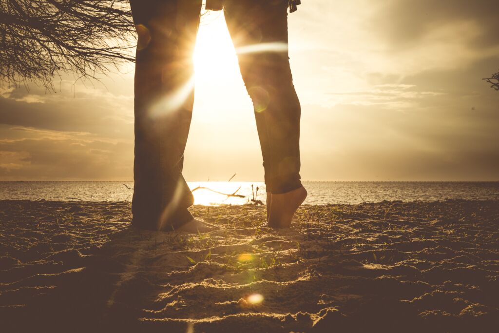Couple standing in the sand with the sun setting between them