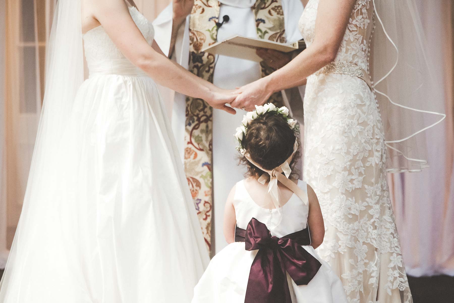 two brides at ceremony with flower girl watching