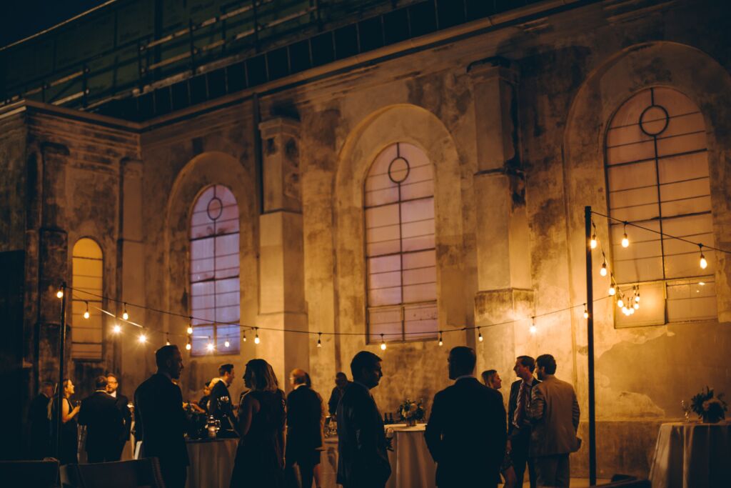 Wedding guests gather during an evening cocktail hour under festoon lights