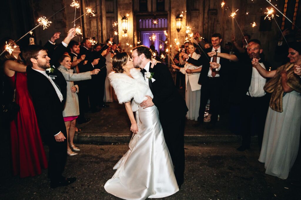 Bride and groom kiss during the exit of their wedding reception with sparklers held by their guests