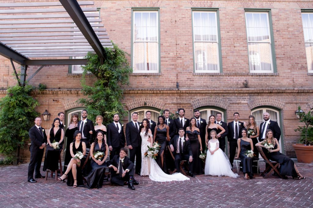 Wedding party of bridesmaids and groomsmen all wearing black and white together in the courtyard of the Hotel Peter & Paul in New Orleans
