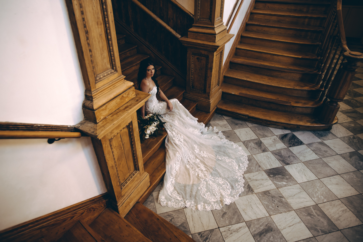 Dramatic bride sits on the main staircase of the Hotel Peter & Paul, her train splayed out across the checkered floor.