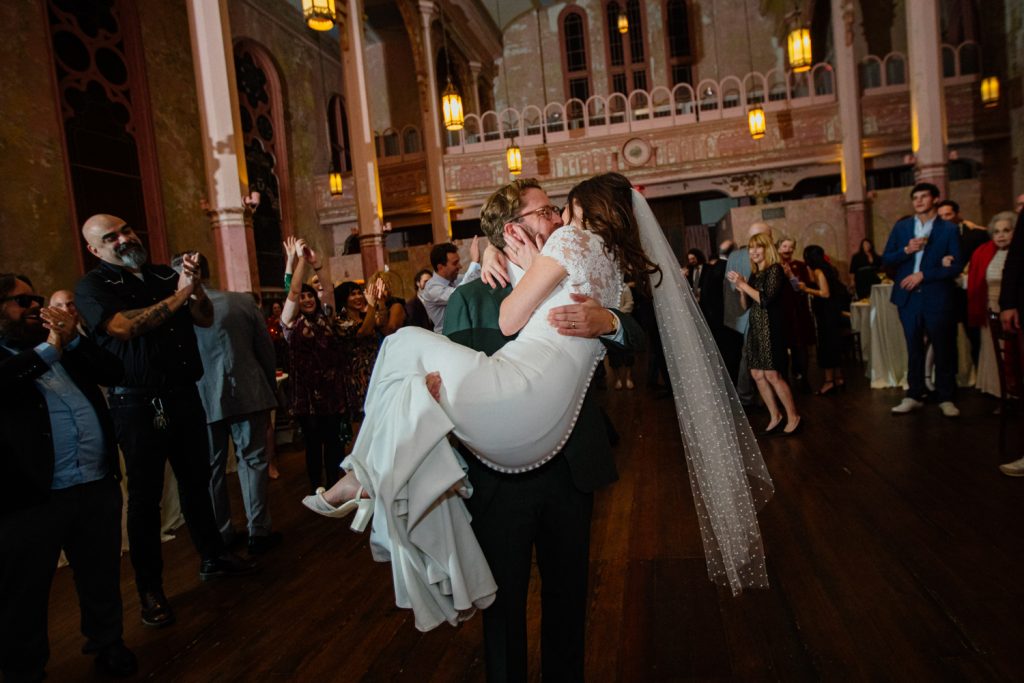 Groom lifts bride on dance floor while wedding guests cheer at Hotel Peter & Paul wedding reception