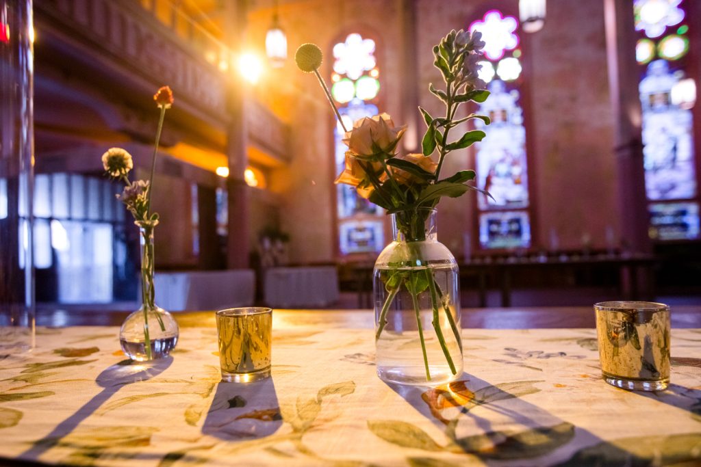 Sunlight pours in through stained glass windows onto simple floral arrangements at Hotel Peter & Paul Church