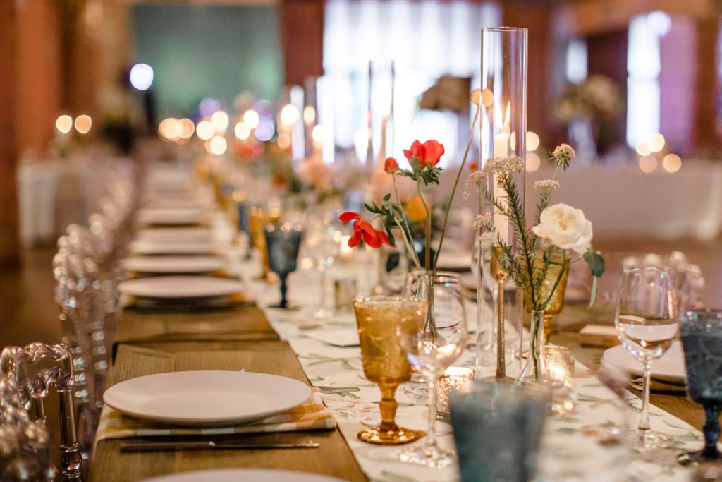 Simple, bright florals adorn long reception table at a wedding reception