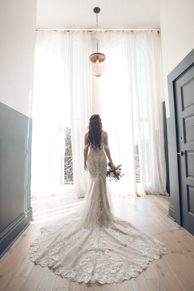 Beautiful bride stands in window light looking out